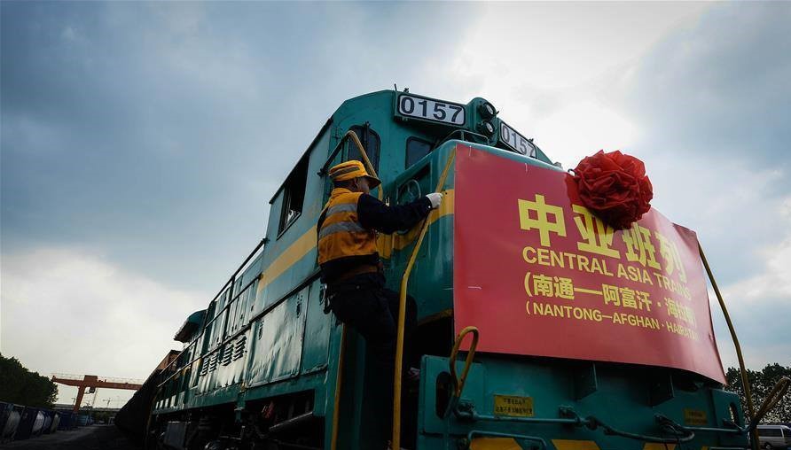 A worker climbs onto a green locomotive decorated with a red banner that reads "Central Asia Train" in English and Chinese.